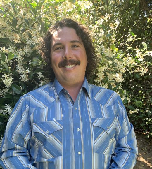 Portrait of Landin Noland in a collared shirt standing in front of star jasmine