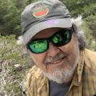 Portrait of Jim Thorne outside, wearing sunglasses and a Davis Farmers Market hat